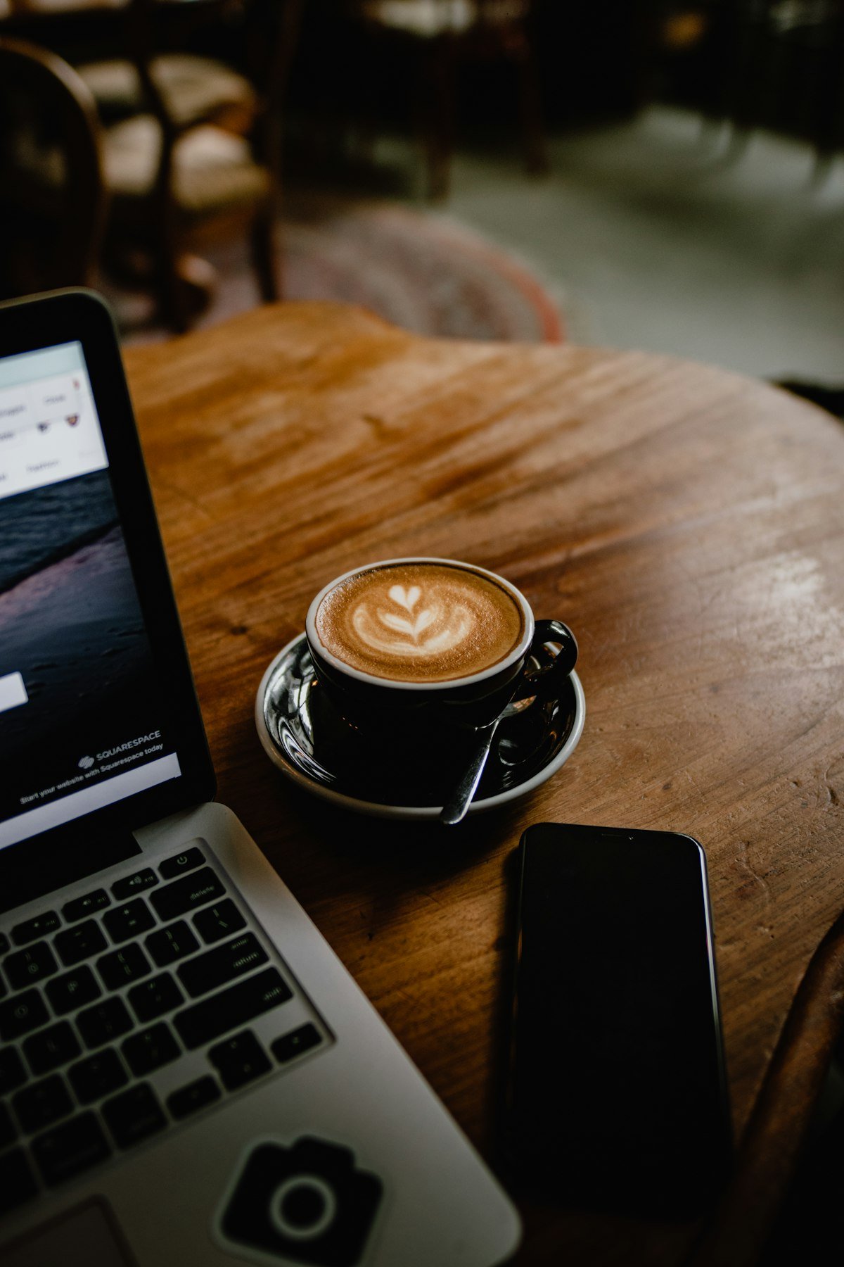 A latte and laptop on a wooden cafe table