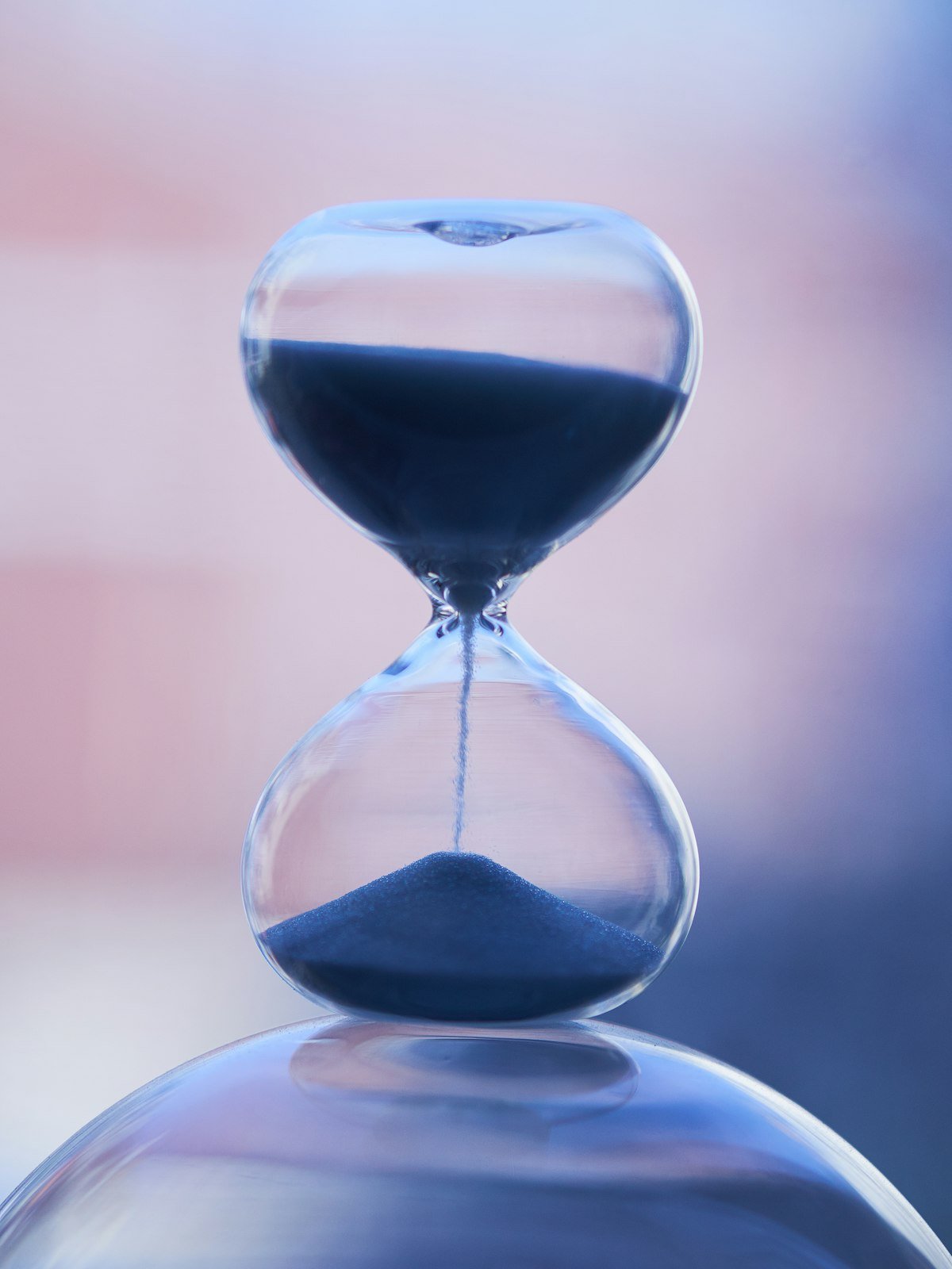 Close-up of a glass hourglass with dark sand flowing through the neck