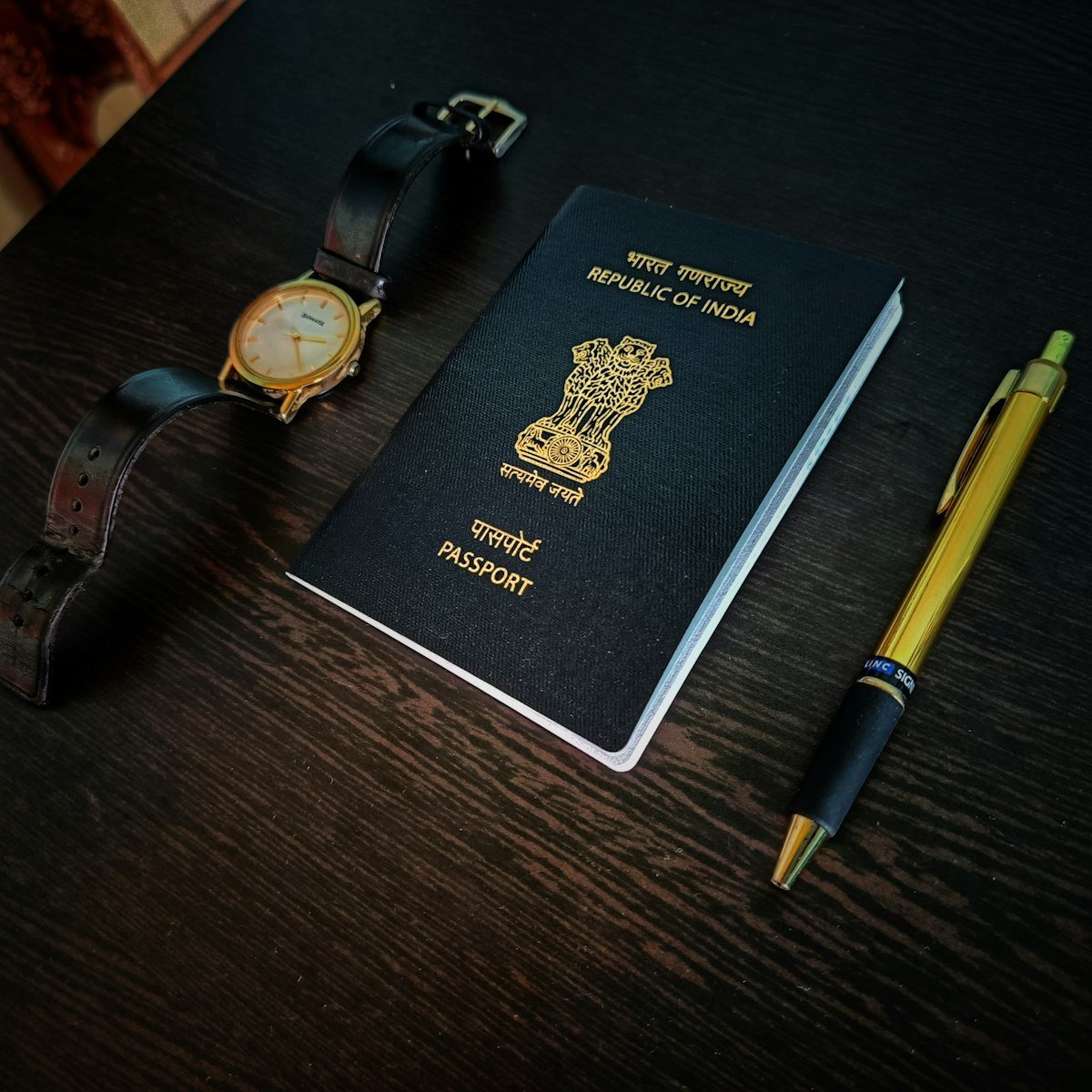 An Indian passport, watch, and pen on a wooden table