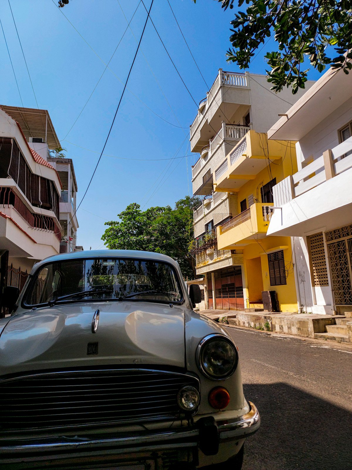 A vintage Ambassador car parked on a street in Pondicherry's French Quarter, with a yellow colonial-era building behind it
