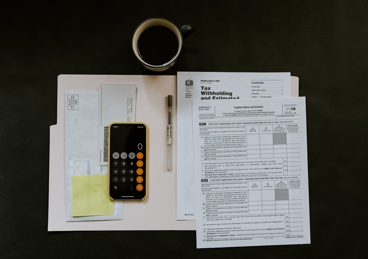 Tax withholding forms, a calculator, and coffee on a dark desk