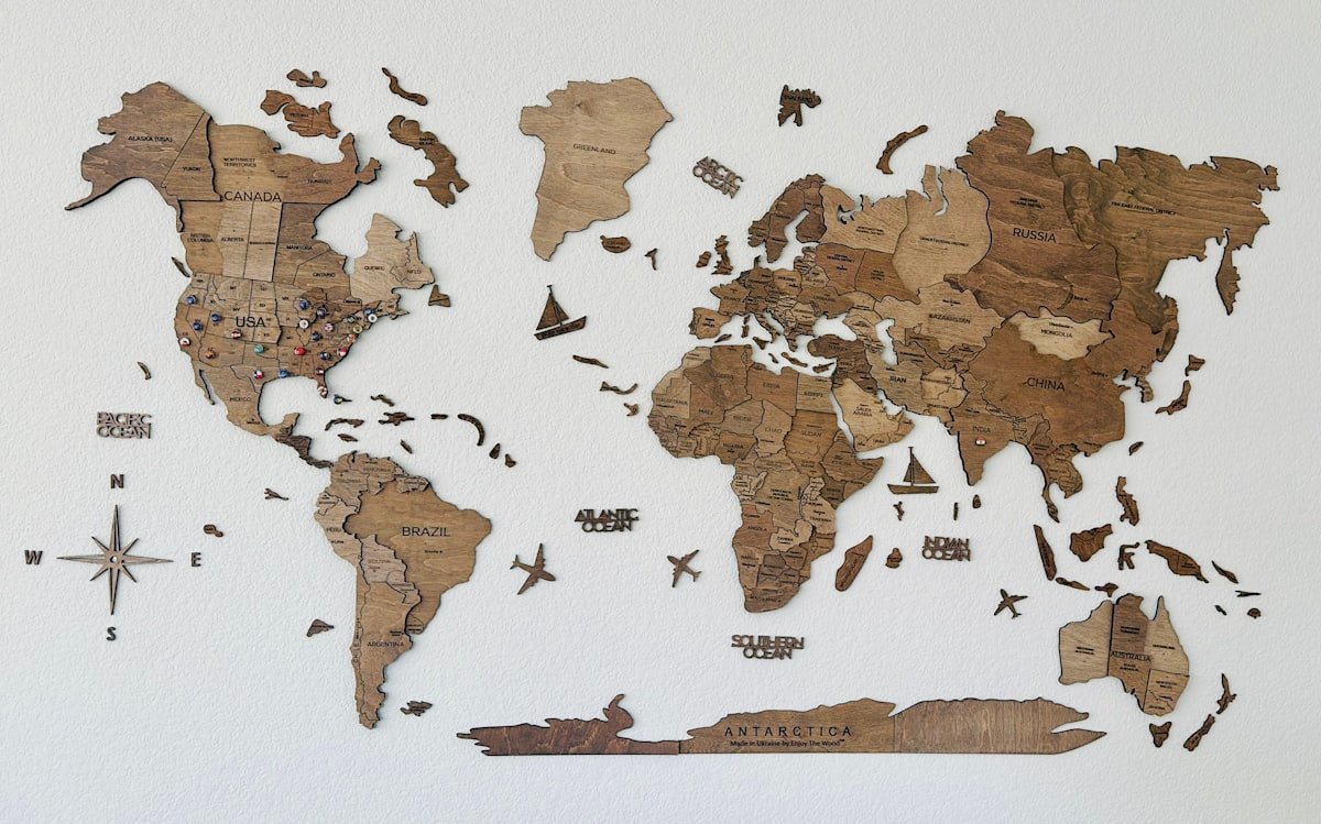 A wooden 3D world map mounted on a wall, showing country borders carved in wood